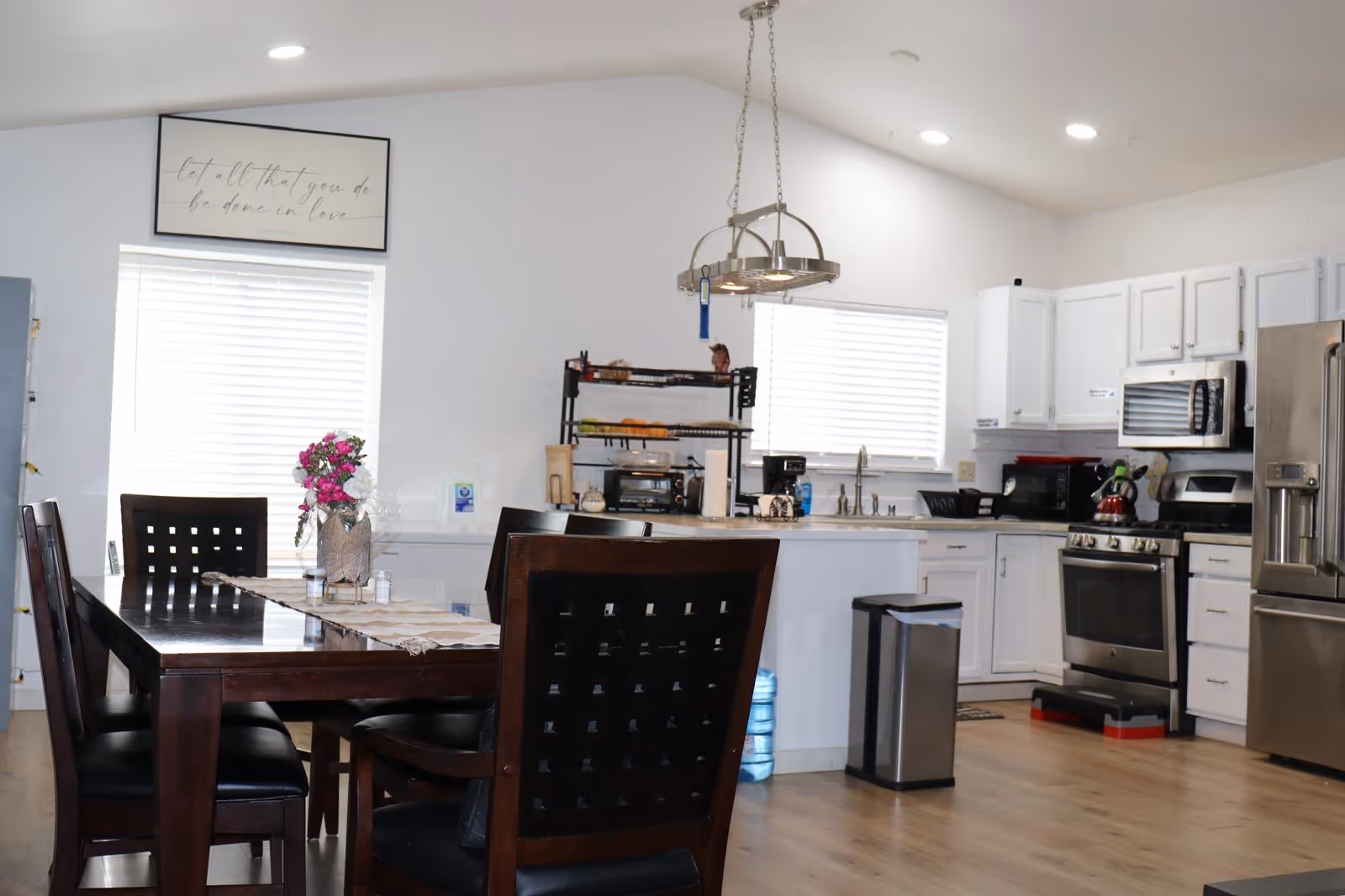 Open dining area features a dark wood table, chairs, flowers, and a white kitchen.