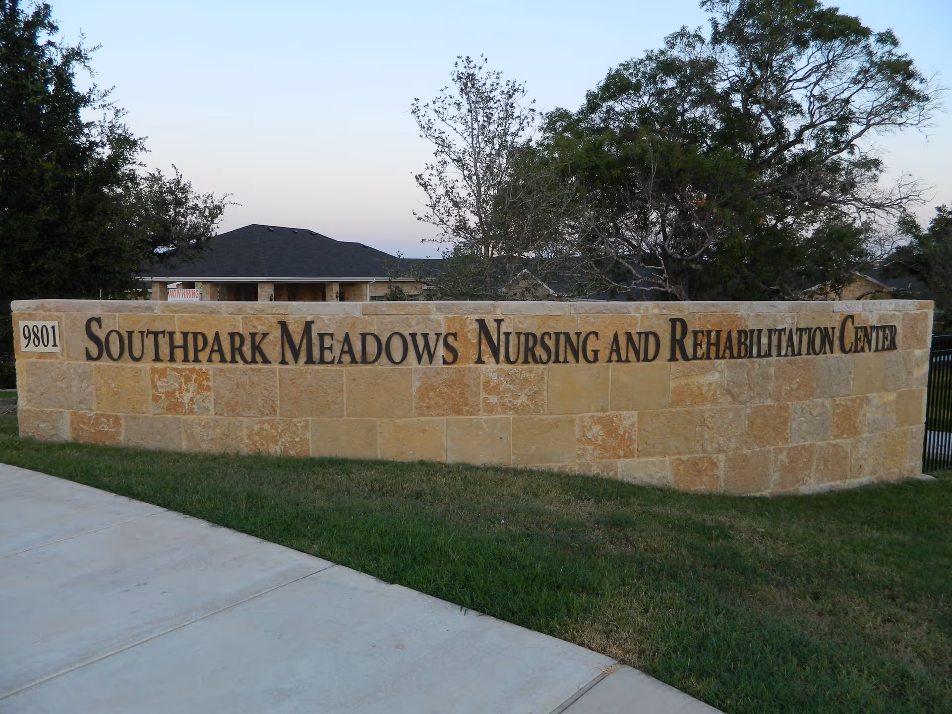 Stone sign with the text 'Southpark Meadows Nursing and Rehabilitation Center' mounted on a low stone wall with grass and trees in the background.
