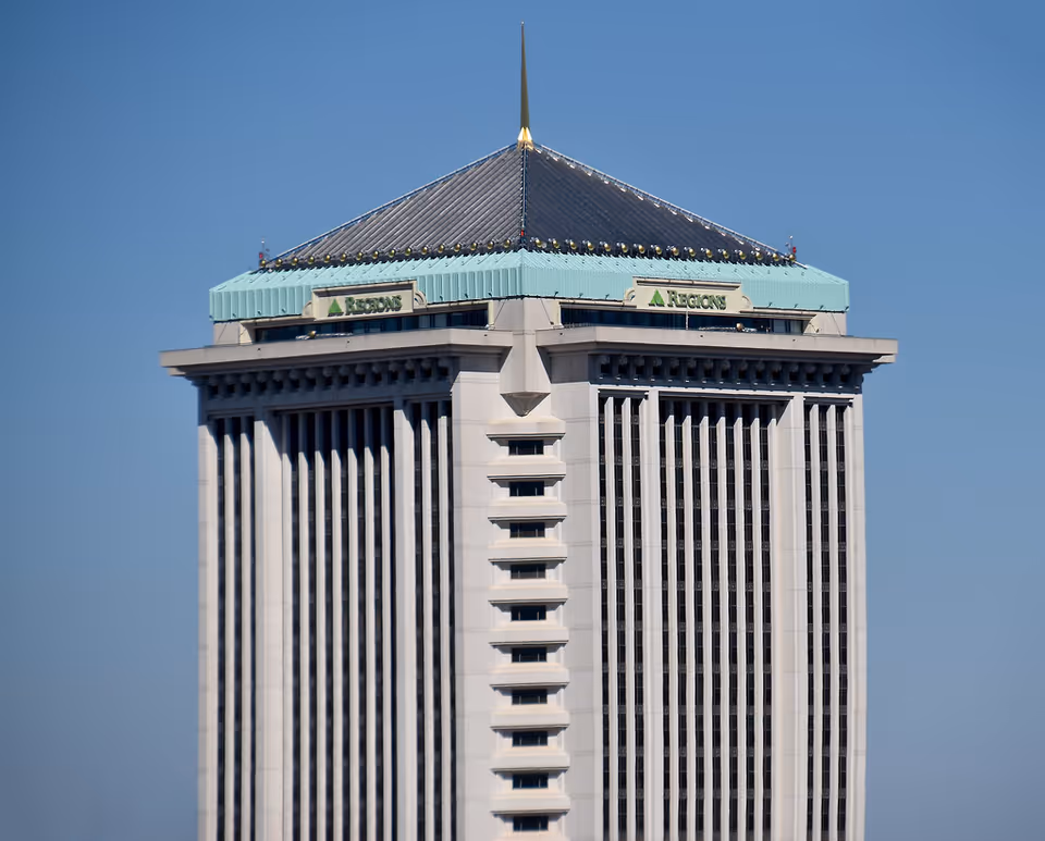 Tall modern high-rise building with a turquoise rooftop and Regions signage under a blue sky.