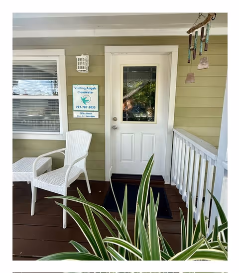 Front porch of Visiting Angels Clearwater with a white chair, door, railing, and plants.