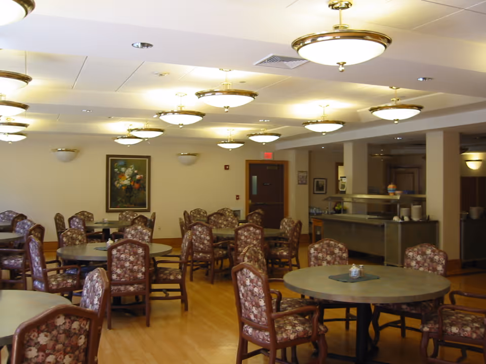 Dining room with multiple round tables and floral-upholstered chairs under ceiling light fixtures.