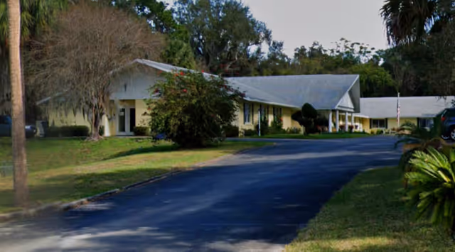 Exterior view of a single-story senior living facility with a driveway and landscaping.