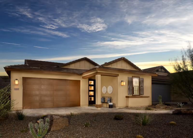 Trilogy at Wickenburg Ranch facility exterior: single-story beige home with garage and desert landscaping at sunset.