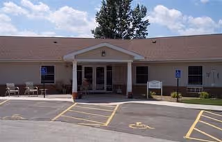 Single-story senior care facility front with a covered entrance, handicap parking, and outdoor seating.