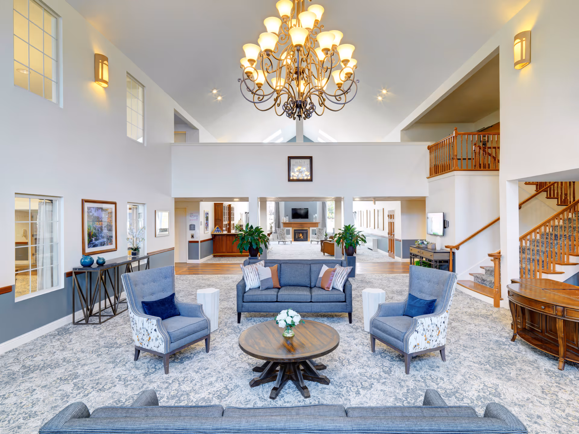Bright, spacious senior living facility lobby with seating area, chandelier, and staircase.