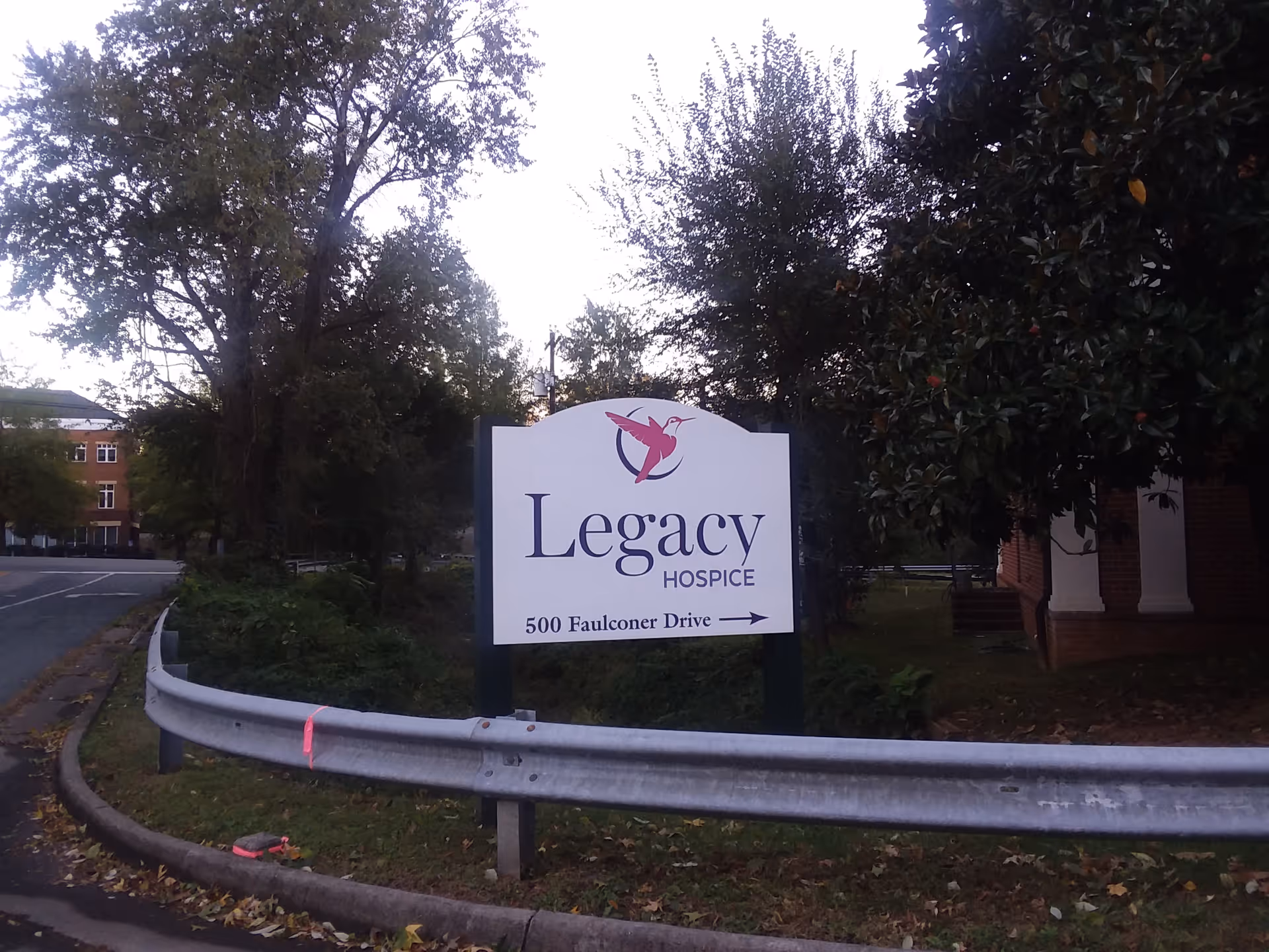 Outdoor scene with a Legacy Hospice sign by a road and trees