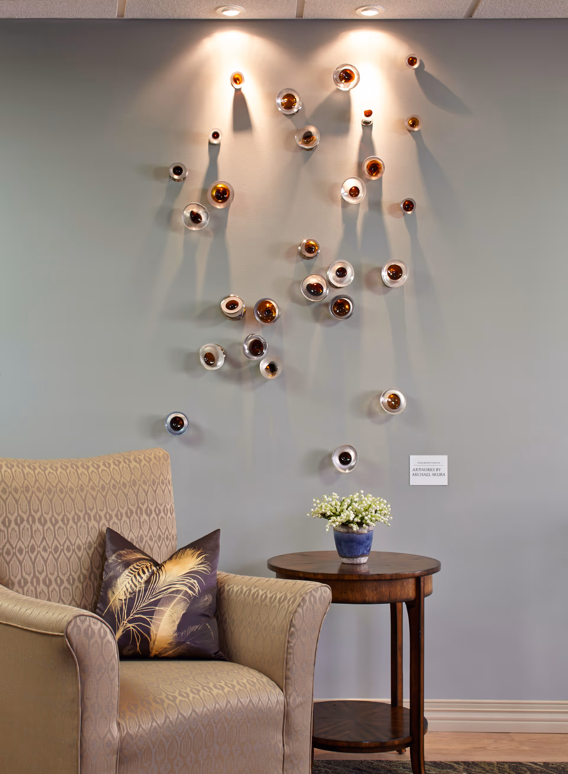 Cozy lounge corner with beige patterned armchair, small round table, and wall-mounted sculptural art.