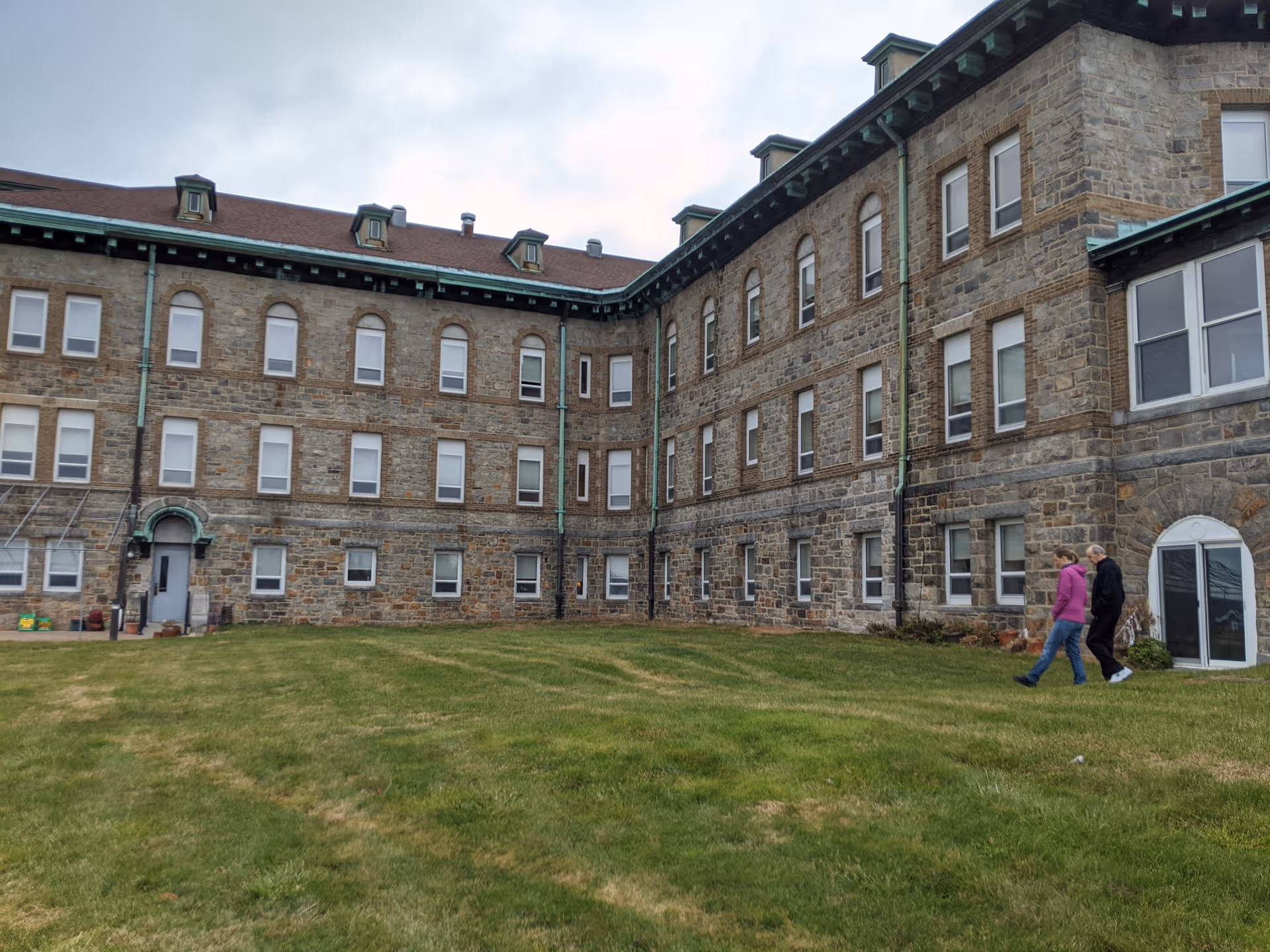 Fairview senior living exterior, a stone building with lawn and two people walking.