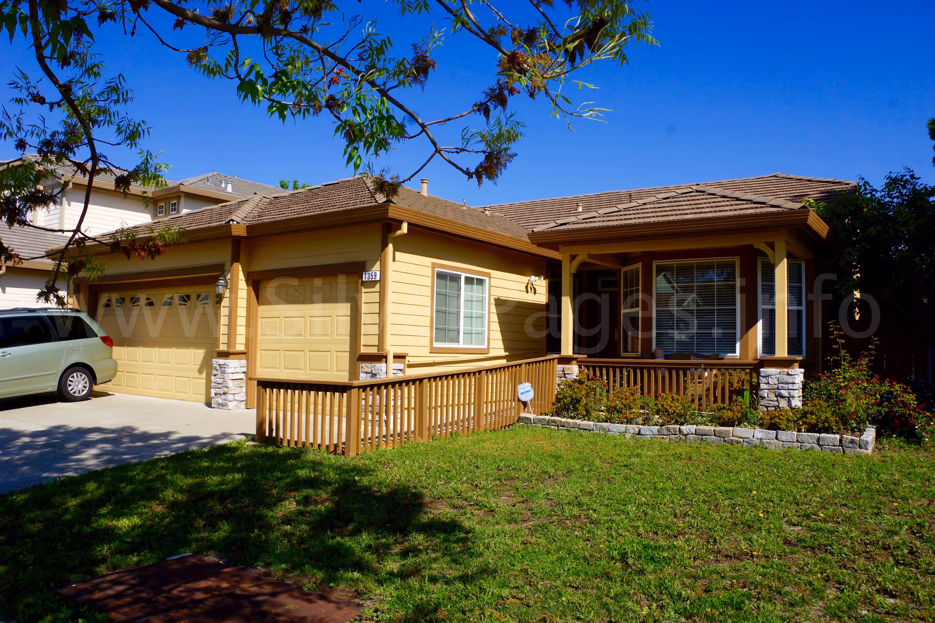 Tan, single-story house with a front porch, attached garage, and landscaped yard.