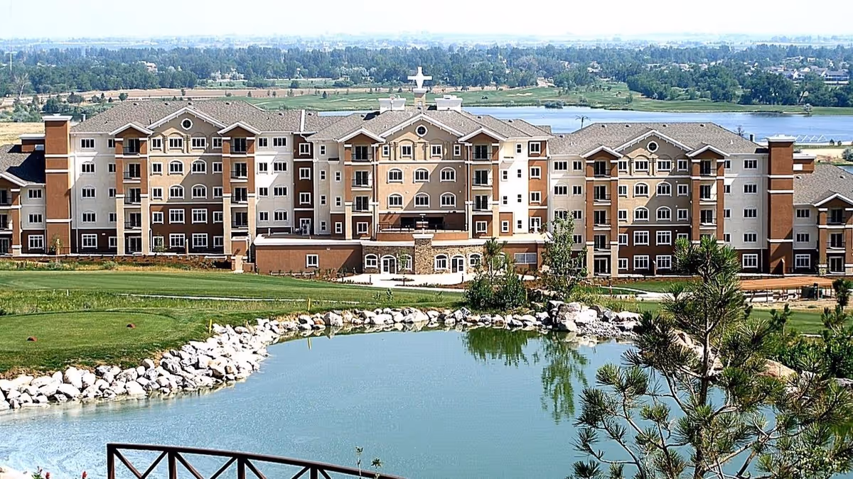 Front exterior view of a large senior living facility with a pond and lawns