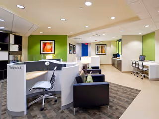 Modern interior lounge and reception area with cubicles, couches, artwork, and computer stations.