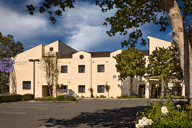 Exterior view of Heritage Park Nursing Center with trees and a parking lot.