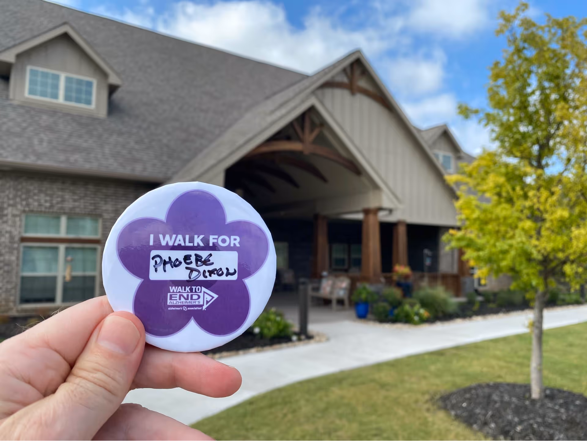 Hand holds a purple flower-shaped sticker in front of Teresa’s House Assisted Living building exterior.