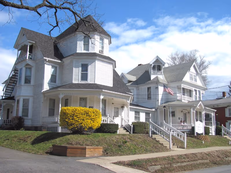 Two white Victorian-style houses with porches and a grassy front yard.