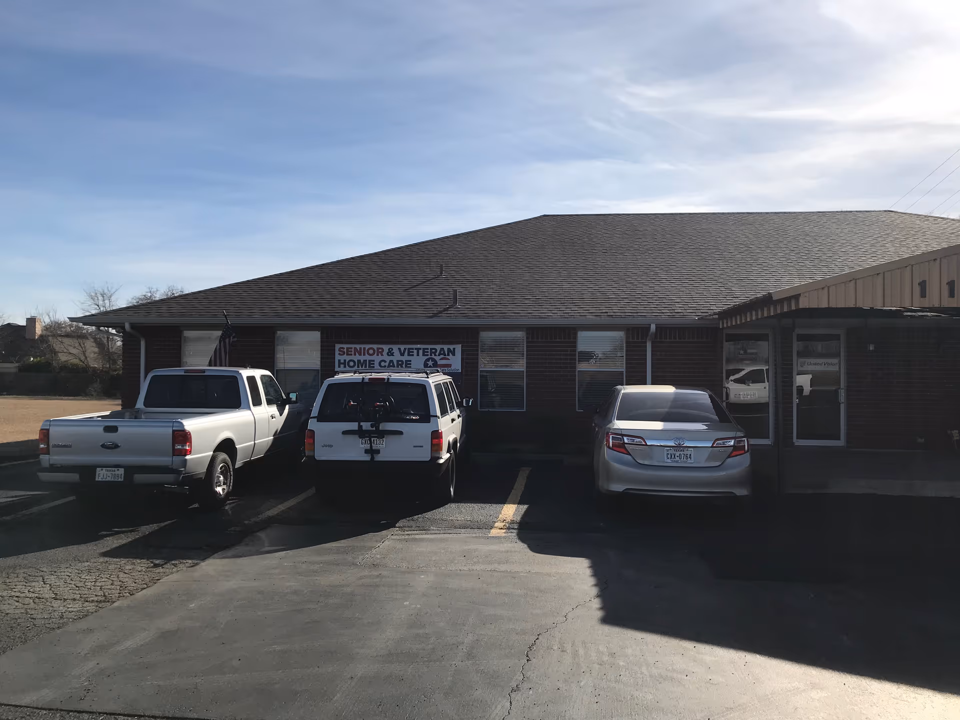 Front view of a brick senior care building with a sign and several parked vehicles.