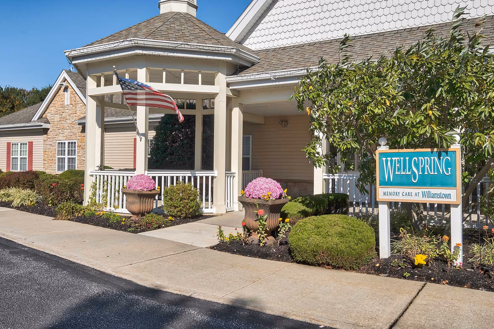 Exterior view of Wellspring Memory Care entrance with porch, flag, and planters.