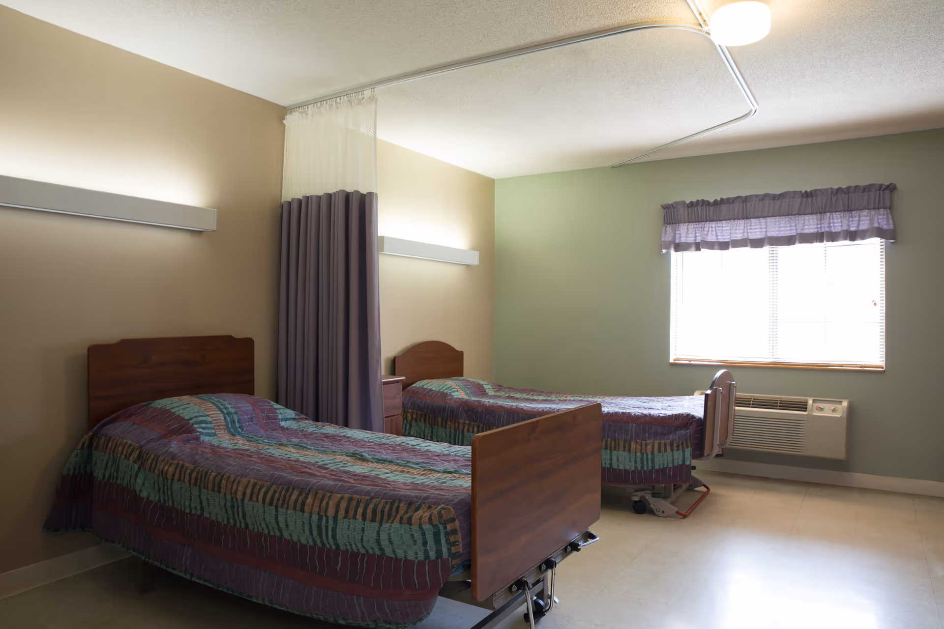 Two single beds with purple striped quilts in a shared senior living bedroom.