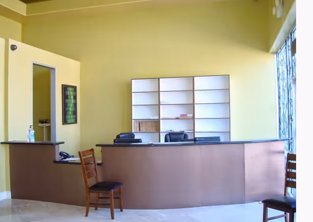 A reception desk with shelves behind and chairs in a lime-green lobby.