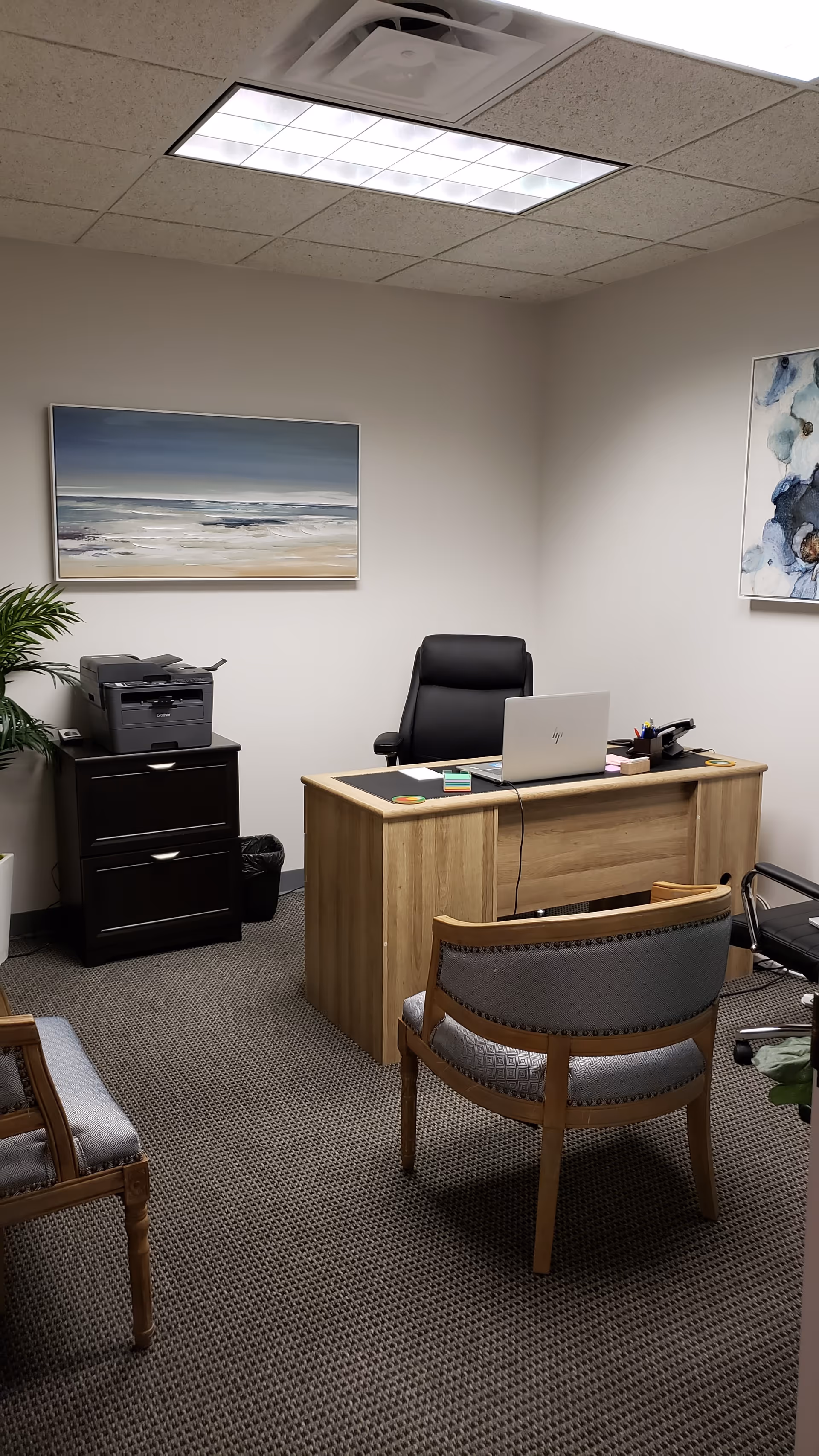 Office reception area with a wooden desk, laptop, printer, and waiting chairs.