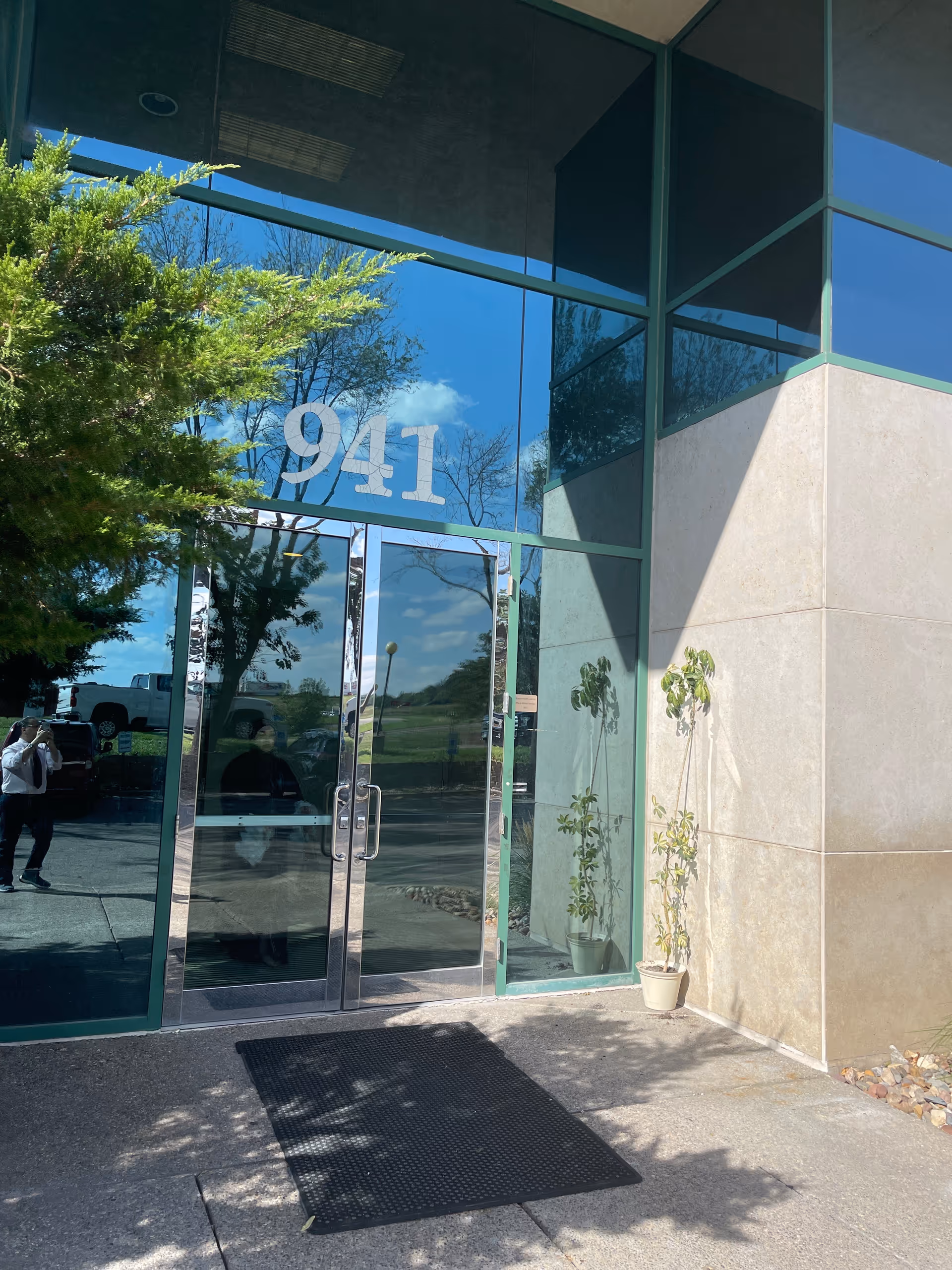Glass-front entrance of a facility with the number 941 and potted plants outside.