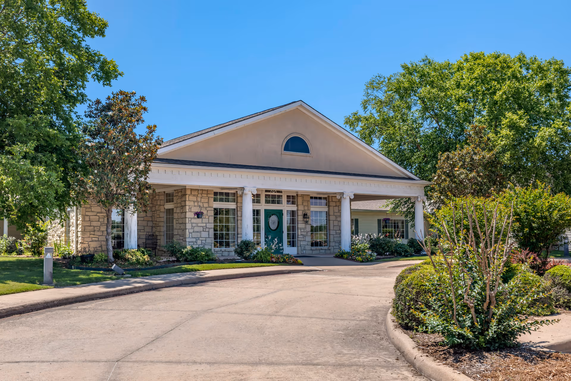 Front view of Country Gardens Assisted Living building with driveway, columns, and landscaped entry.