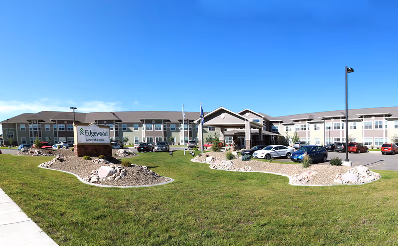 Exterior view of Edgewood Mandan senior living facility with entrance and parked cars.