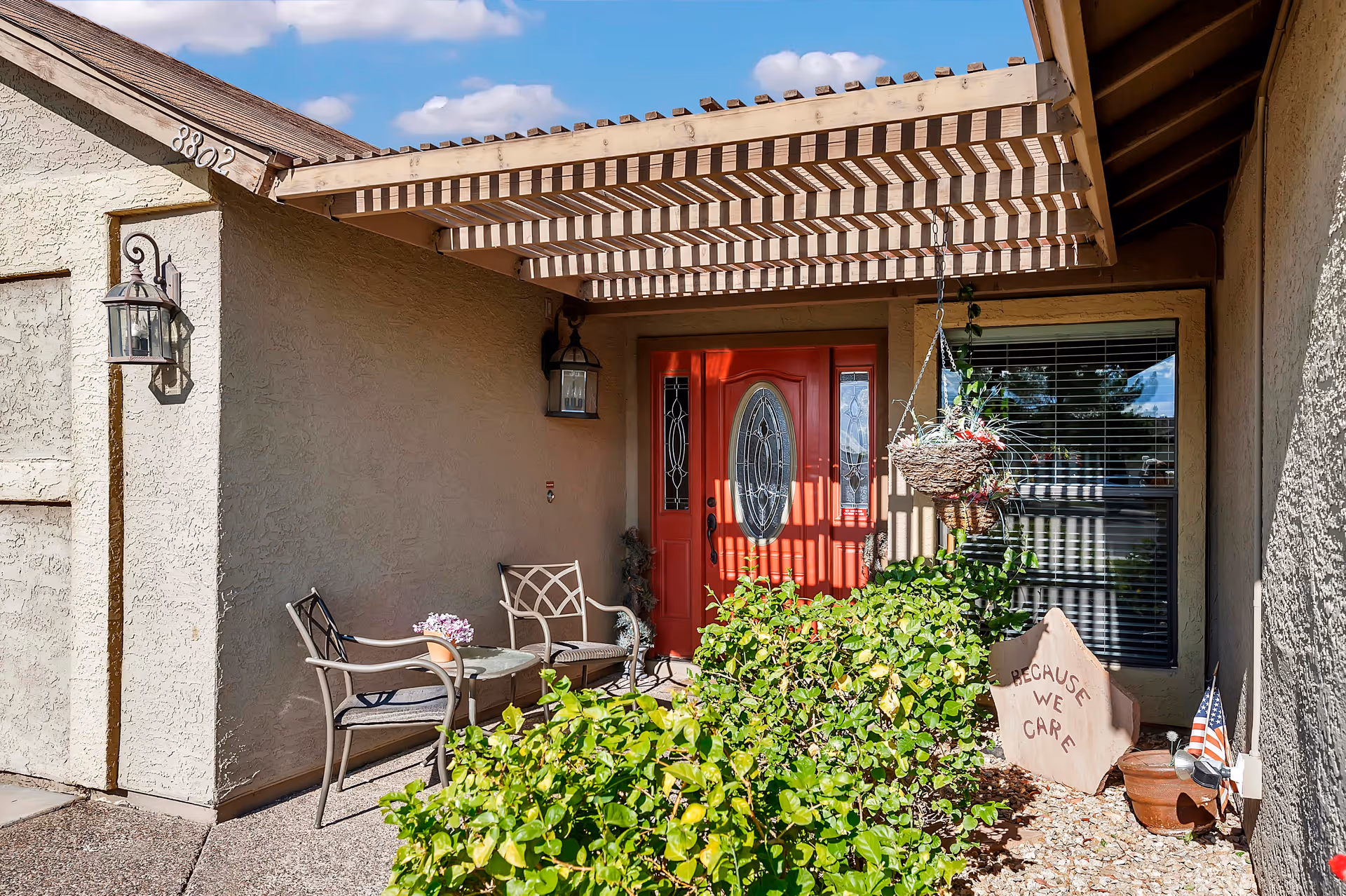 Front entry with a red door, porch seating, hanging planter, and desert landscaping.