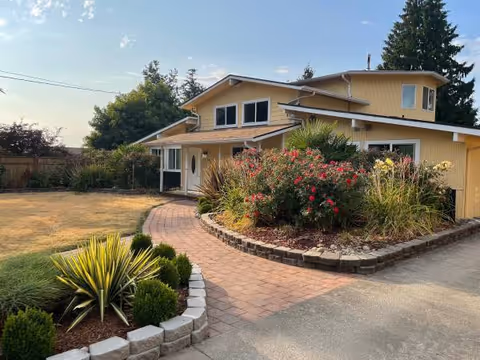 Front view of a yellow senior care home with a curved brick walkway and garden.