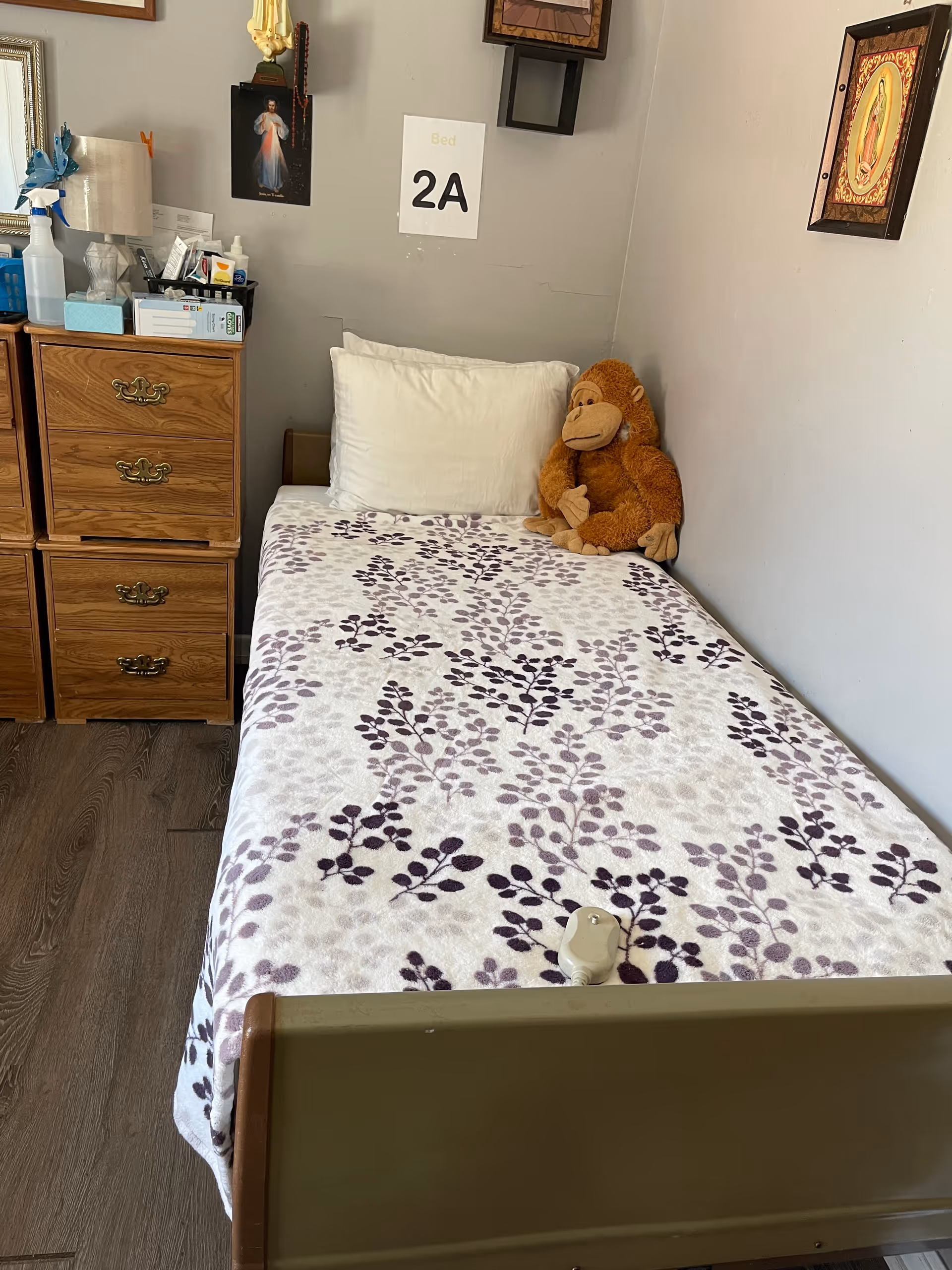 A single-bed resident room with floral blanket, stuffed monkey, and dresser.
