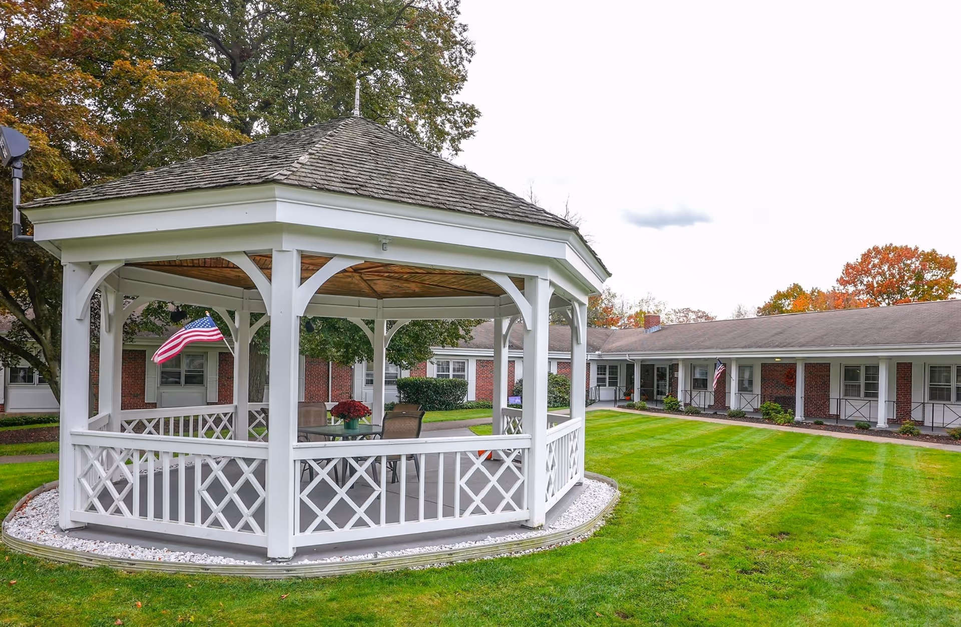 White gazebo in a manicured lawn courtyard beside a brick senior housing building.