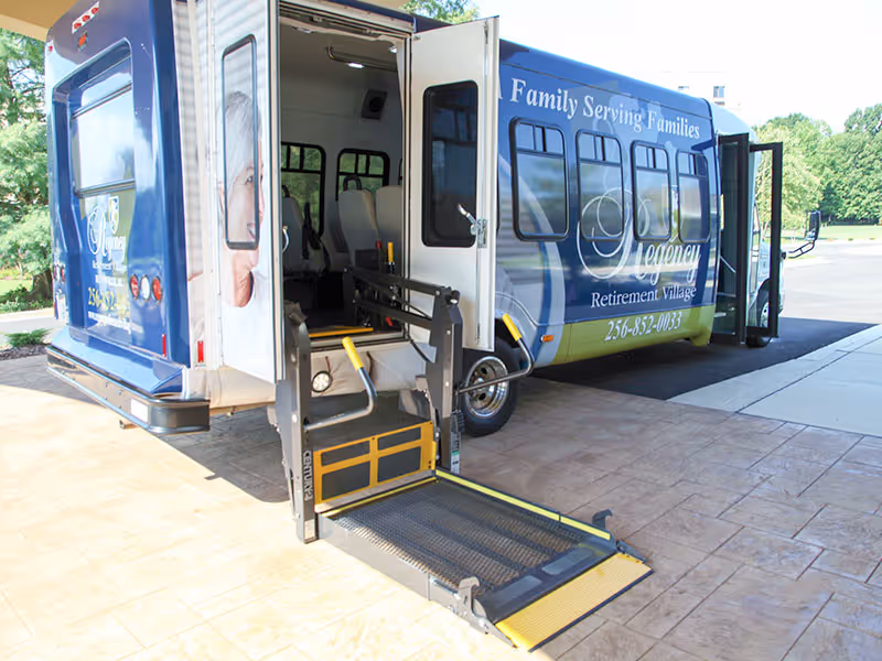 A Regency Retirement Village shuttle bus parked outside with its wheelchair lift extended at the entrance.