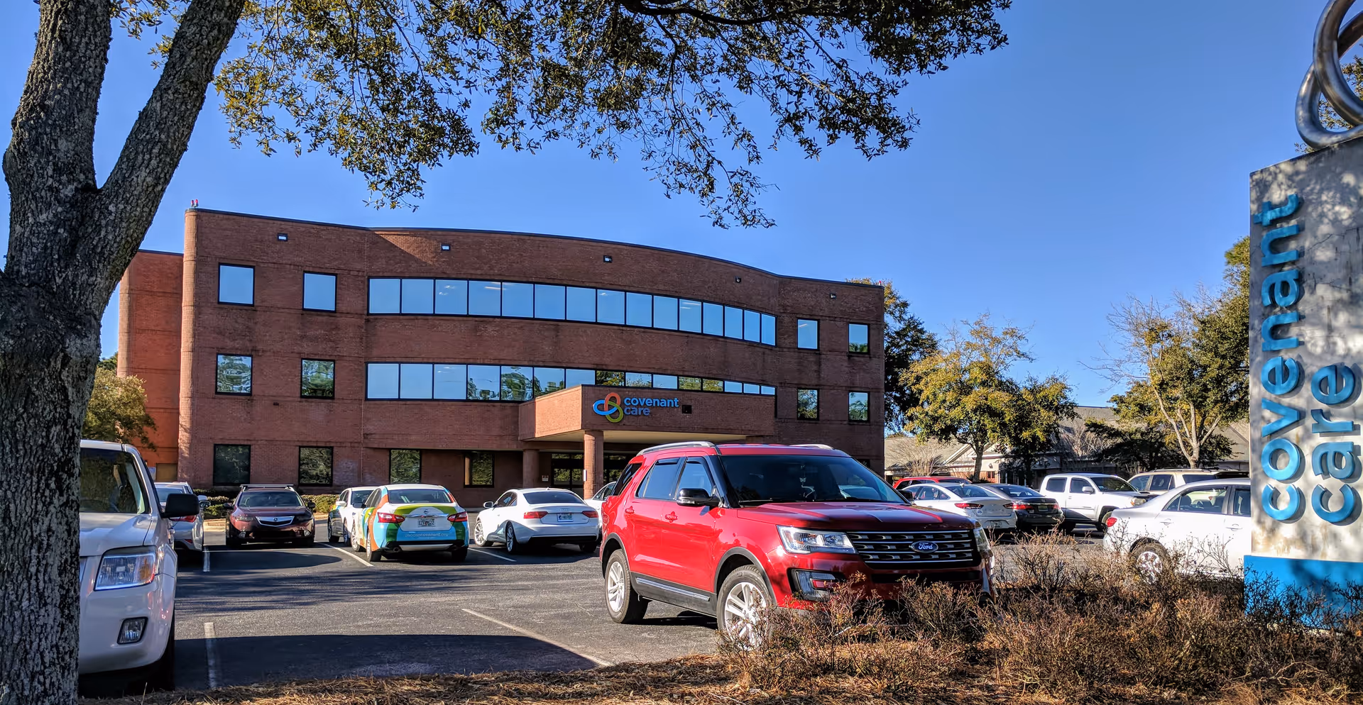 Red brick Covenant Care building with a parking lot in front and a blue sky