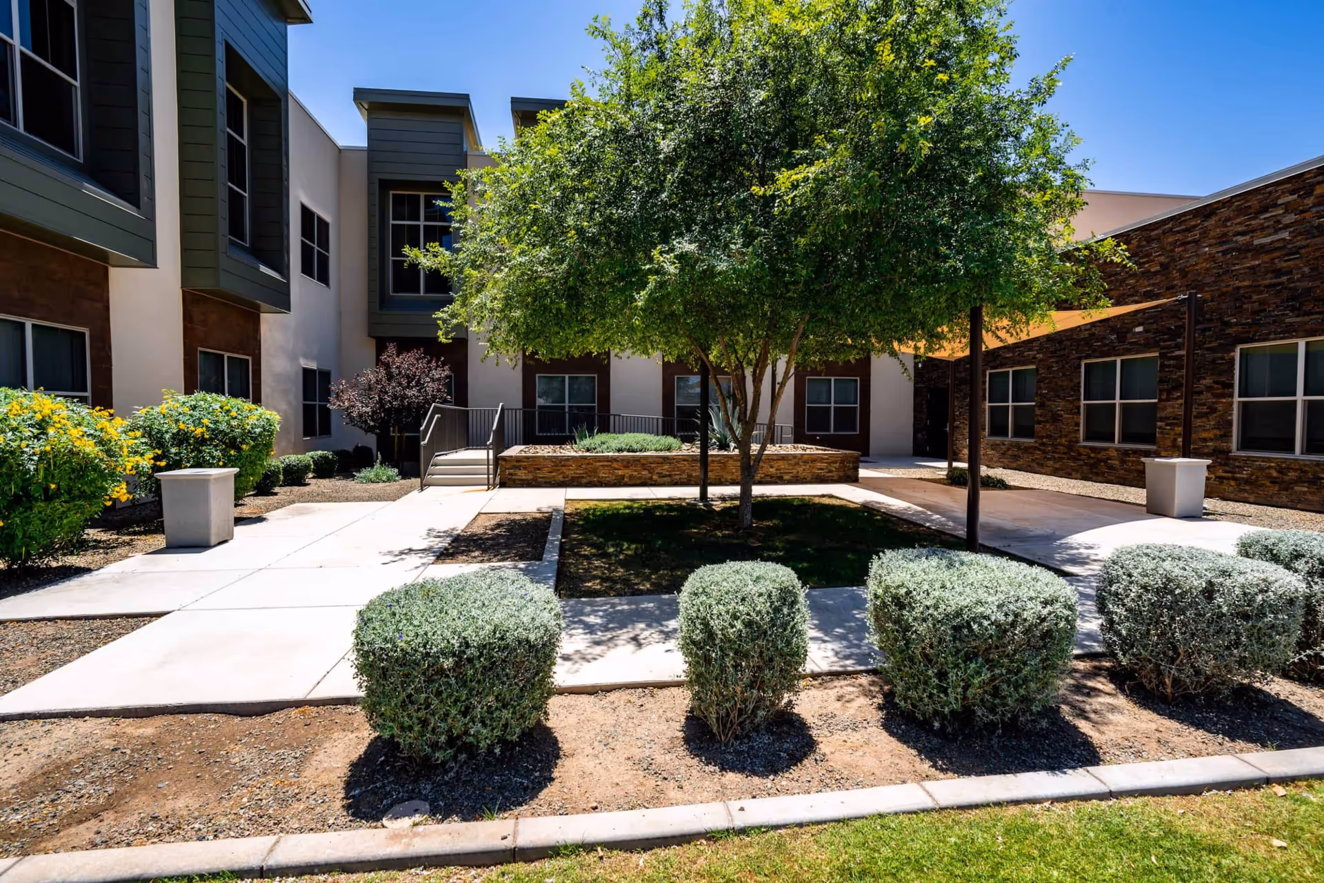 Exterior courtyard at Fairmont of Farmington Hills with trees, shrubs, and walkways.