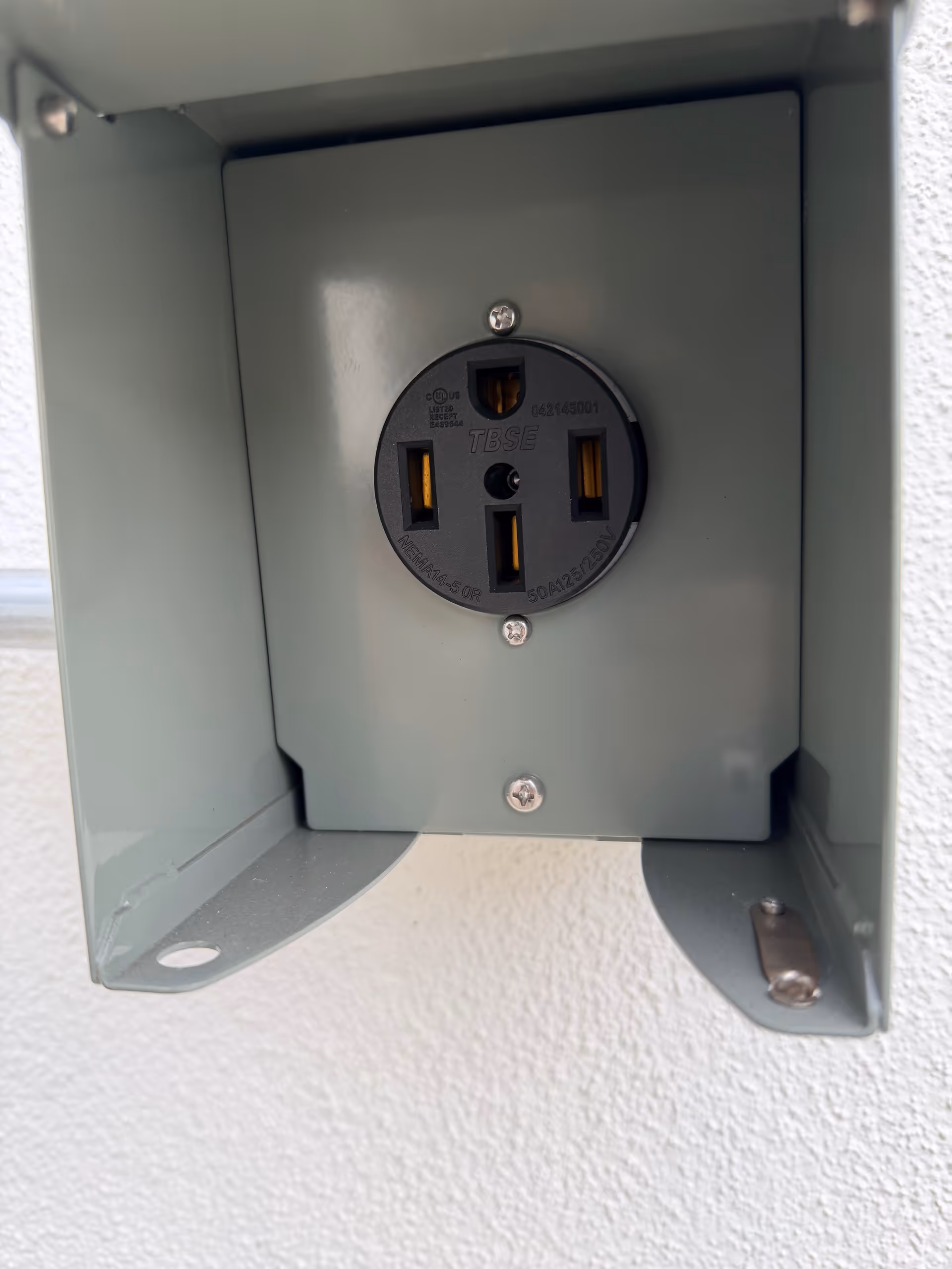 Close-up of a gray weatherproof outdoor electrical outlet mounted on a wall.