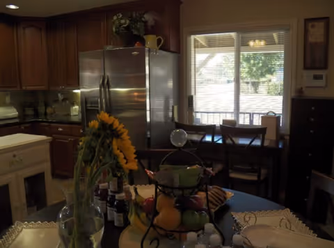A cozy interior kitchen and dining area with wooden cabinets, a stainless refrigerator, and fruit centerpiece.