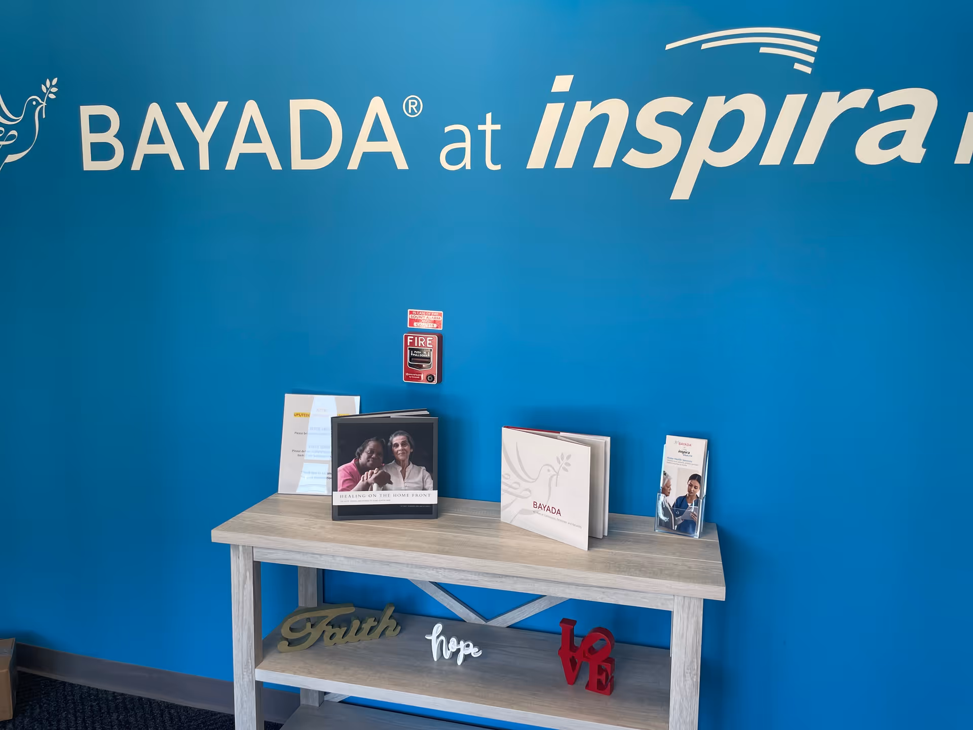 Blue wall with BAYADA at Inspira sign behind a wooden brochure table.
