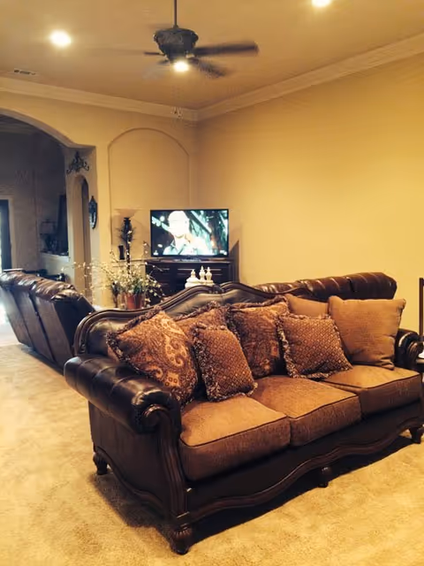 Cozy living room with a brown leather sofa, cushions, and a TV in a homey setting.