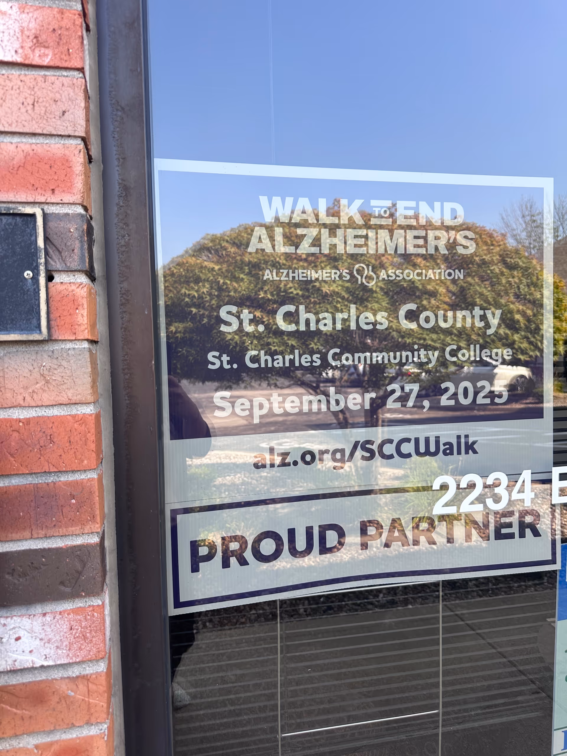 Glass storefront window displaying Walk to End Alzheimer's event text beside brick wall