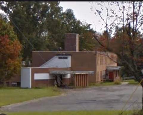 Exterior view of Amor Residential Care Home building with driveway and trees in front.