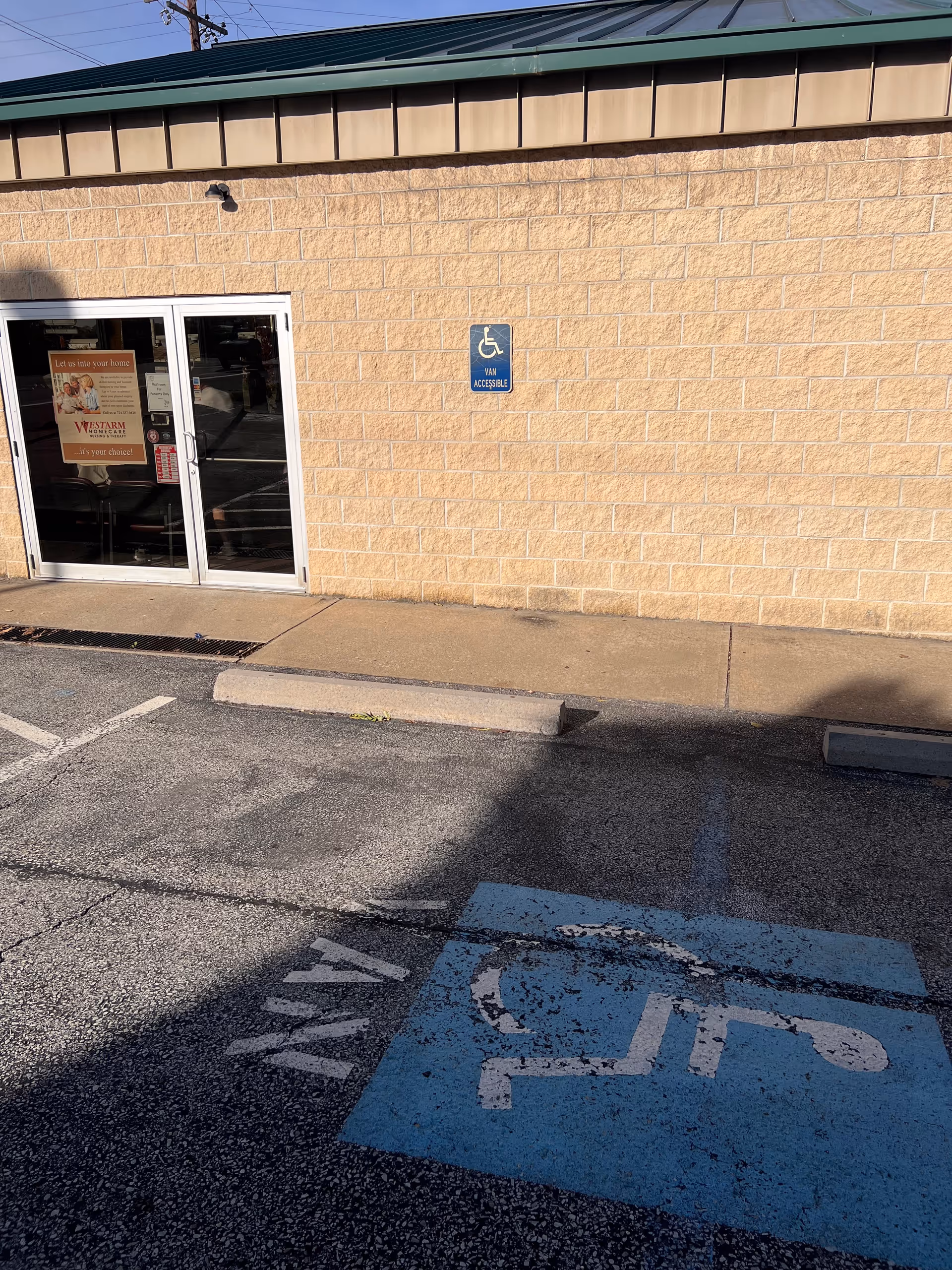 Exterior view of a beige brick building with glass entrance and handicap parking.