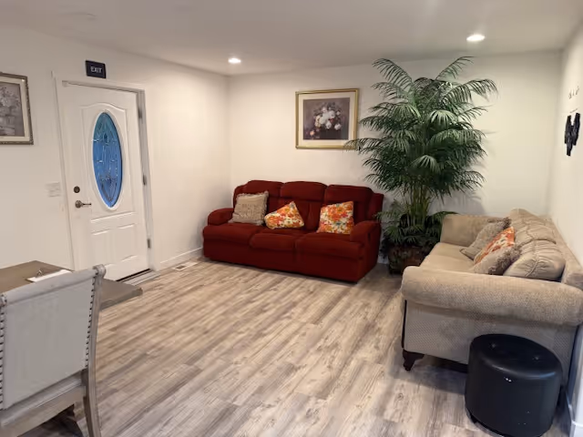 Bright living room with red and beige sofas, plant, and artwork.