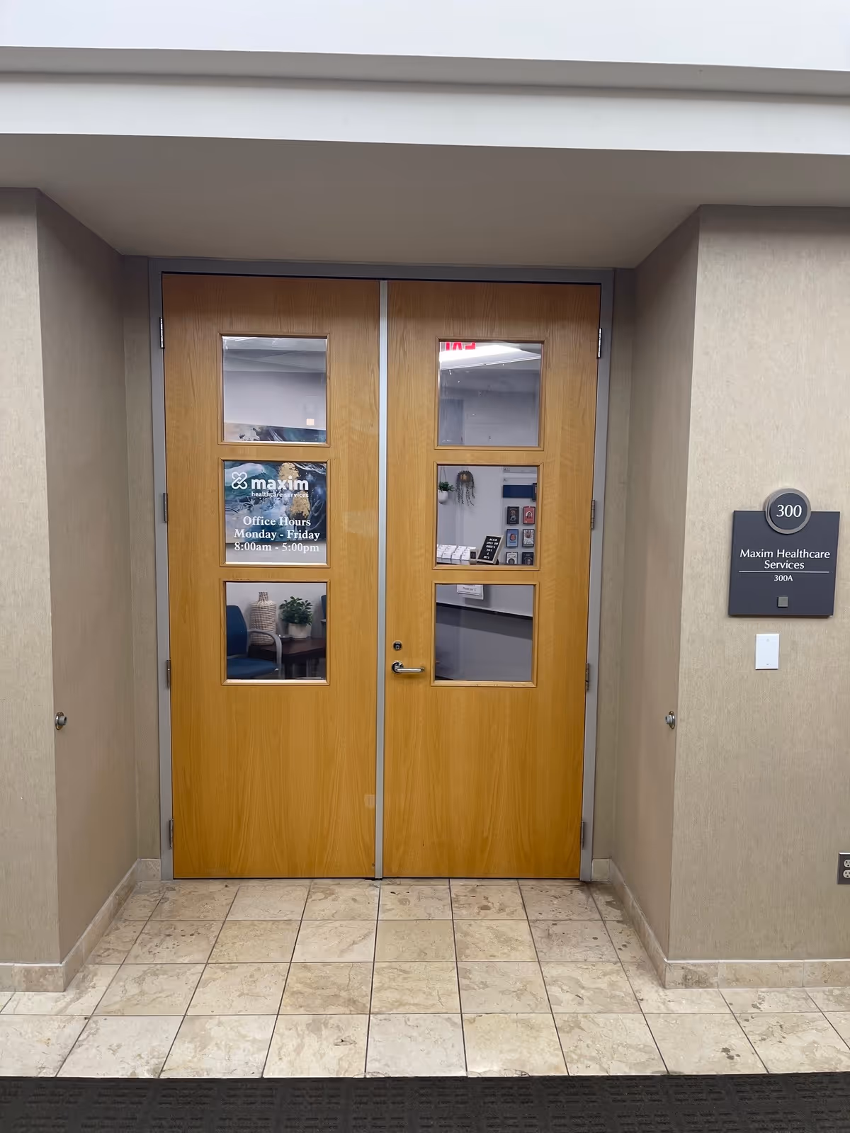 Double wooden doors with glass panels in a tiled hallway, signage for Maxim Healthcare