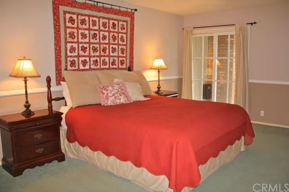 Bedroom with a large bed, red quilt, two nightstands, and a sliding glass door.