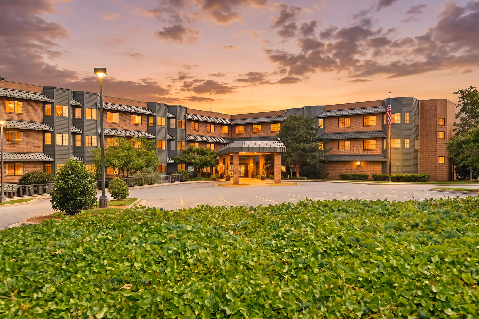 Sunset sky over Heritage Woods Senior Living building with brick exterior and manicured greenery.