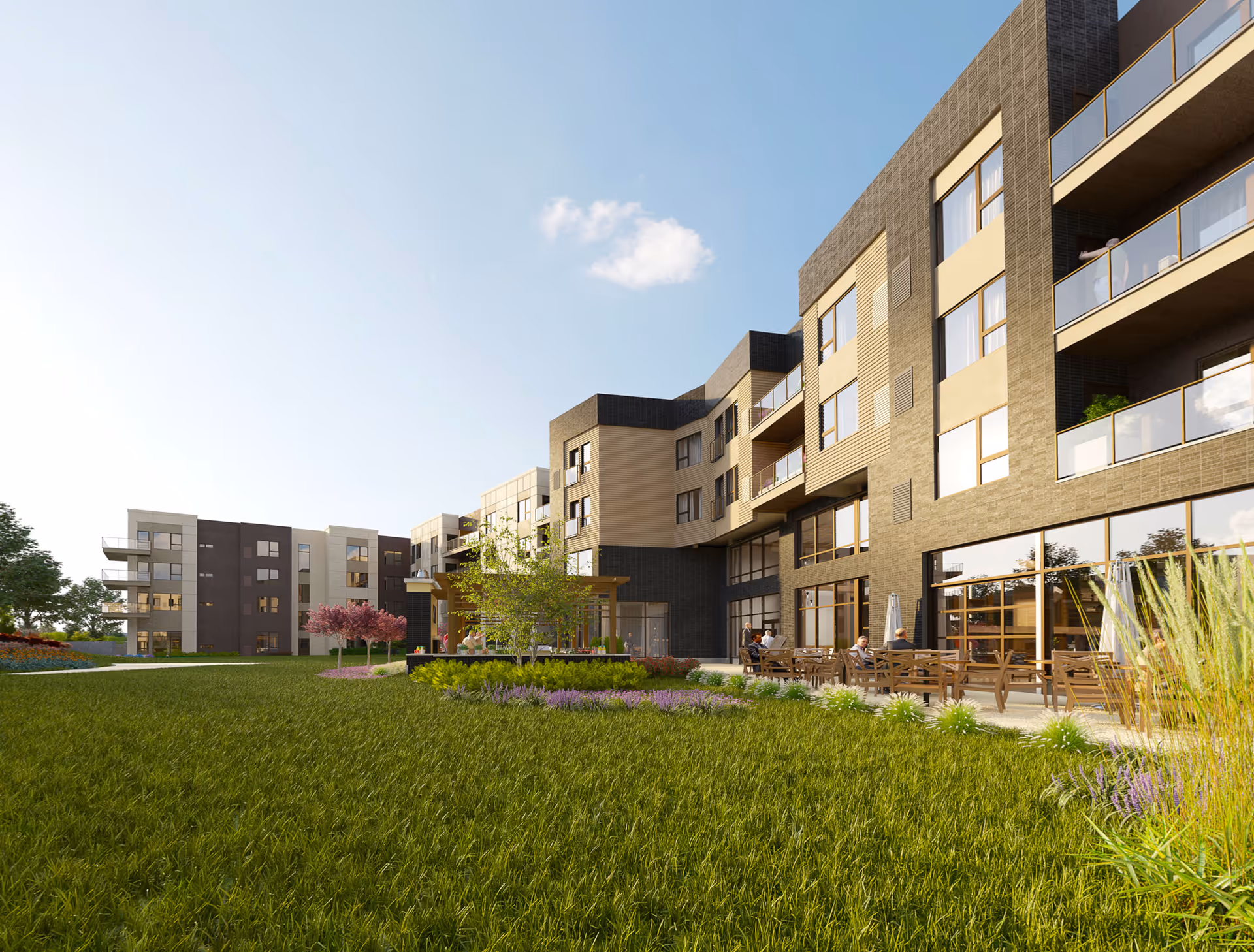 Exterior view of a modern multi-story senior living facility with large windows and balconies. The building is surrounded by a well-maintained lawn and landscaped garden with flowering plants and small trees. Several people are seated on outdoor benches and chairs near the building under a clear blue sky.