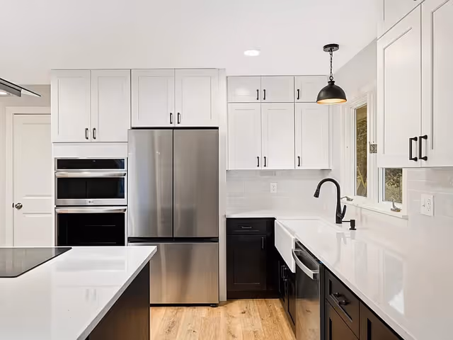Modern white kitchen with stainless steel refrigerator, island, and black faucet in bright space.