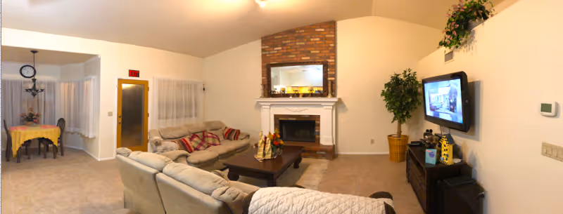 Senior living facility living room with fireplace, couches, coffee table, TV, and dining area.