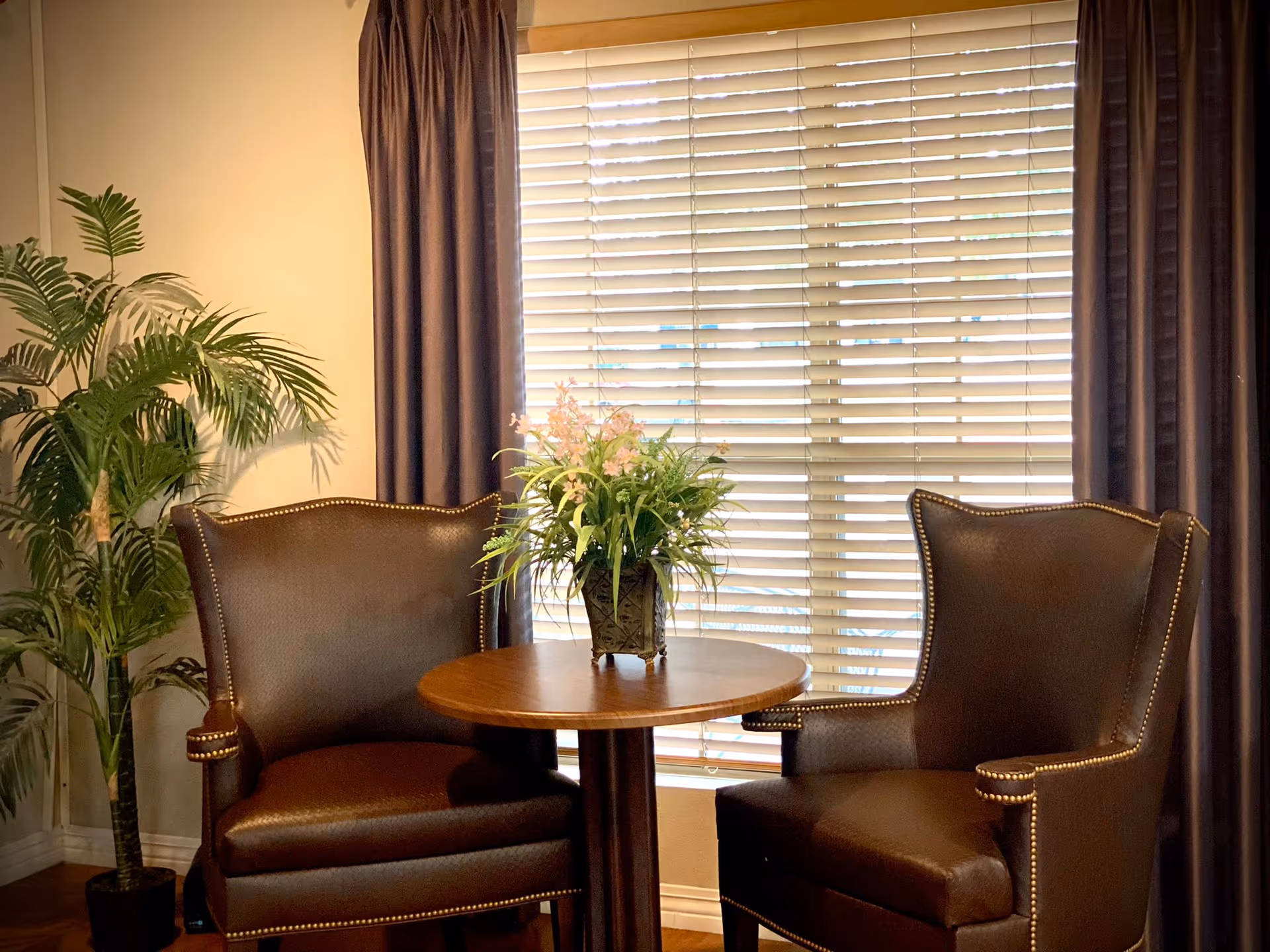 Two brown leather chairs sit around a round table with a flower centerpiece.