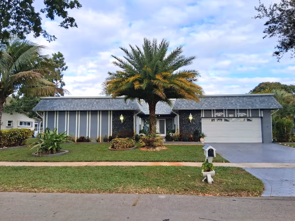 Front view of a single-story senior living home with palm trees and a two-car garage.