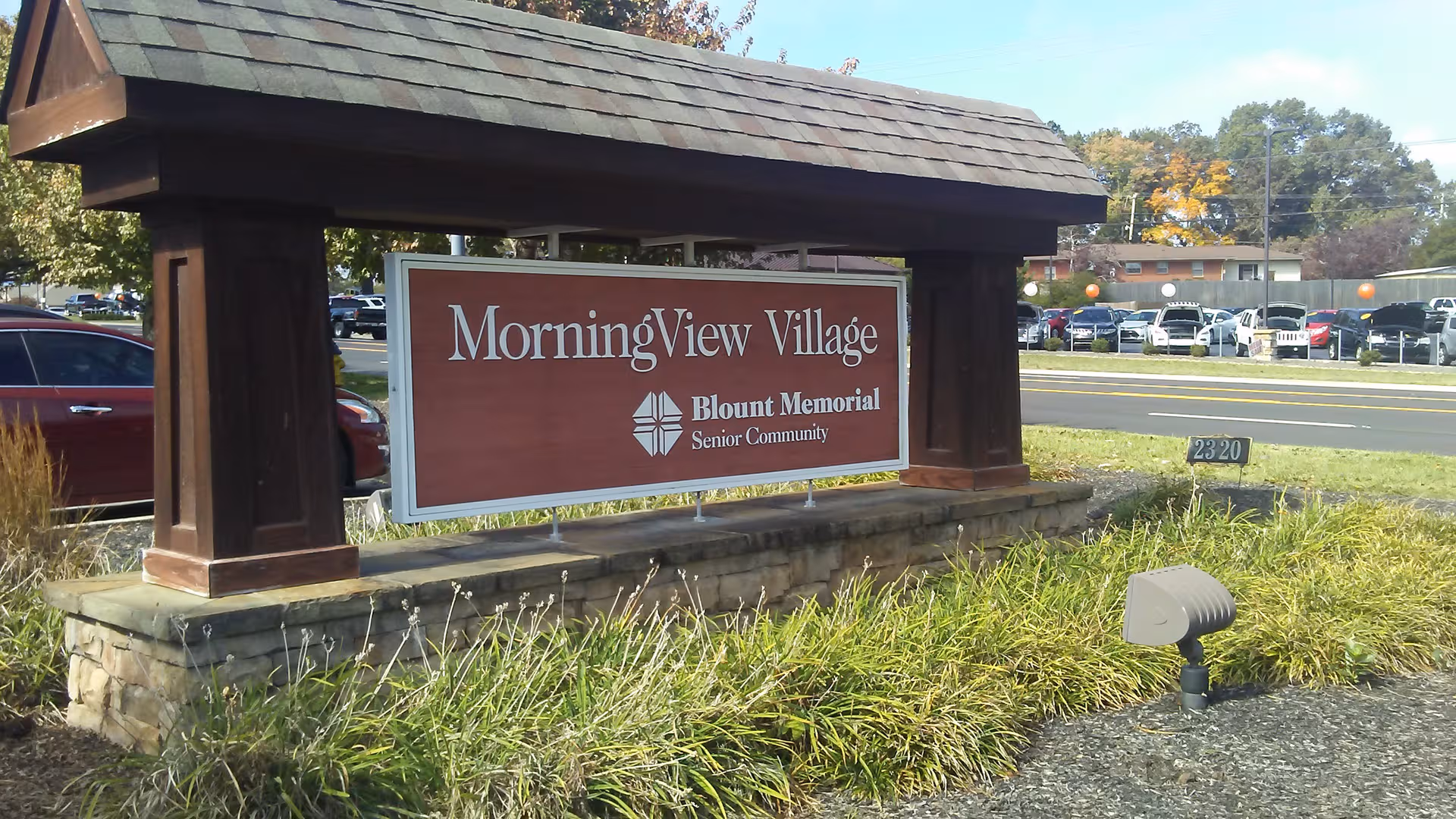 Large wooden entrance sign reading MorningView Village Senior Community beside a parking lot.